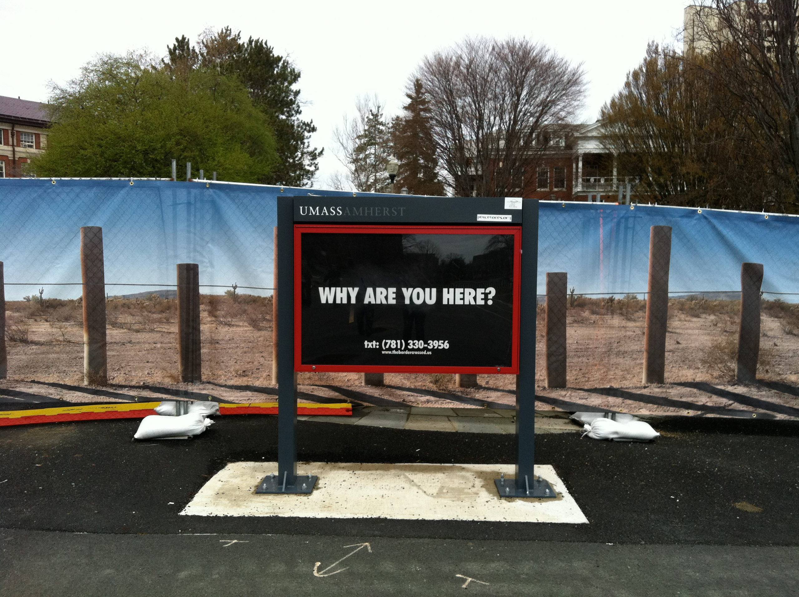 An black board against against an image of the southern border wall in the USA, asking 'Why are you here?'